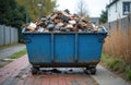 Blue metal bin on wheels filled with construction debris like bricks and concrete. Container sits on paved surface with grass and Royalty Free Stock Photo