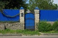 A blue metal door with a black forged pattern and a wall of a fence Royalty Free Stock Photo