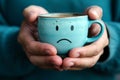 Blue monday concept. Hands with a blue cup of cappuccino with a sad face Royalty Free Stock Photo