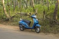 Blue motorbike stands on the asphalt road against the green jungle