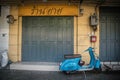 A blue motorcycle parked in front of an antique shophouse with wooden doors in Bangkok