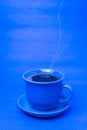 Blue mug with steaming hot coffee. Soft smoke. Blue background.