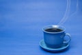 Blue mug with steaming hot coffee. Soft smoke. Blue background.