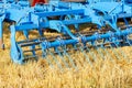 A multi-row cylindrical metal harrow in blue against a harvested yellow field in sunlight. Closeup Royalty Free Stock Photo
