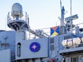 The blue Nato logo on a side of a large gray modern warship with radars and weapons. Naval exercises, attack and defense. Close-up