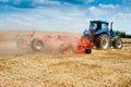 Blue new tractor with red harrow in the field against a cloudy sky, agricultural machinery work raises dust Royalty Free Stock Photo