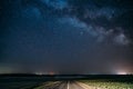 Blue Night Starry Sky Above Country Asphalt Road In Countryside And Green Field. Night View Of Natural Glowing Stars And Royalty Free Stock Photo