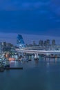 Blue night view on circular highway leading to the Rainbow Bridge with Cargo and cruise ships moored or sailing in Odaiba Bay of