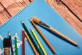 Blue notebook and various colored pencils and brushes on a wooden table Royalty Free Stock Photo