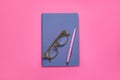 Blue office notebook, eyeglasses and pen on pink, top view Royalty Free Stock Photo