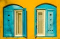 Blue old style wooden windows, symmetry in open doors, yellow house wall background in small town, minimal style of simplicity, Royalty Free Stock Photo