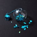 Blue painted leaf in a glass vase and dry rose painting blue on a black paper background. Royalty Free Stock Photo
