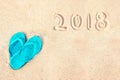 Blue pair of flip flops on the beach, 2018 written in the sand