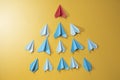 Blue paper aeroplane origami following rhe red one on yellow background