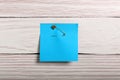 Blue paper note attached with safety pin to white wooden background, top view Royalty Free Stock Photo