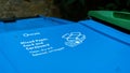 A blue paper recycling trash can in a garden with instructions on the lid