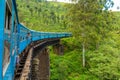 A blue passenger train moves through the jungle of Sri Lanka