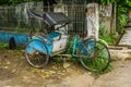 Blue pedicap or tricycle parked in side of the road near bush and wall with nobody around photo taken in Depok Indonesia