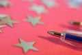 A blue pen lies next to the silver stars on a pink background. Grade system and school performance. Ratings and comparisons