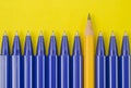 Blue pens and one yellow pencil on yellow background.