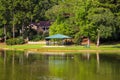 A blue pergola near vast silky green lake water surrounded by lush green trees and grass with mallard ducks Royalty Free Stock Photo