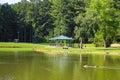 A blue pergola near vast silky green lake water surrounded by lush green trees and grass with mallard ducks and Canadian geese Royalty Free Stock Photo