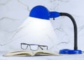 A blue personal sized desk lamp on a marble desk in front of a marble Royalty Free Stock Photo