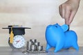 Blue piggy bank with stack of coins money and Graduation hat on Alarm clock on wooden background, Saving money for education Royalty Free Stock Photo