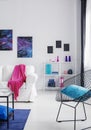 Blue pillow on black stylish metal armchair in bright cosmos inspired interior with white furniture, real photo with copy space on