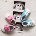 Blue and pink booties next to baby photos with ultrasound in 4th week of pregnancy. Twins. Son and daughter. Selective focus.