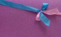 Blue and pink ribbons in the shape of a bow on a purple background. Congratulatory postcard. Copy space Royalty Free Stock Photo