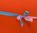 Blue and pink ribbons in the shape of a bow on a red background. Congratulatory postcard. Copy space, Royalty Free Stock Photo