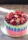 Blue, pink and violet striped cake with melted chocolate, fresh cheeries, strawberries, raspberries and mini donuts Royalty Free Stock Photo