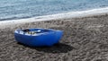 Blue plastic boat on black sand at the beach