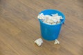 A blue plastic bucket filled with used tissues sits on a wooden floor Royalty Free Stock Photo