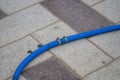 Blue plastic hose for irrigation on outdoor pedestrian tiles, connected from two halves with metal clamps and a pipe Royalty Free Stock Photo