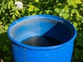 Blue, plastic water barrel reused for collecting and storing rainwater for watering plants partly emptied during summer day