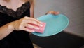 Blue plate with pink dish sponge in hand on blurred background Royalty Free Stock Photo