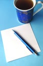 Blue porcelain china cup with blue pen and pencils, white note card and blue background Royalty Free Stock Photo