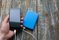 Blue power bank with white usb and black smartphone in the hand on old vintage wooden background. Modern, information technology Royalty Free Stock Photo