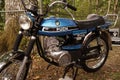 Blue Puch motorbike parked in a lush forest environment