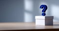 Blue question mark symbol standing on white closed box on wooden surface with blurred background Royalty Free Stock Photo