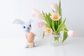 Blue rabbit holds one egg next to a bouquet of tulips in a glass jar. The conceptual of Easter