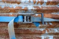 A blue rachet strap wrapped around a rusty corrugated iron metal sheet