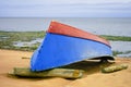 A blue-red boat lies upside down on the sandy seashore Royalty Free Stock Photo