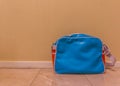 Blue with red messenger school bag isolated in against a wall and standing on the floor in a room Royalty Free Stock Photo