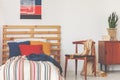 Blue, red and orange pillows on single bed with stripped duvet and wooden headboard in oldschool bedroom interior, real photo