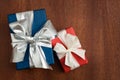 A blue and a red present with silver and white bow on a wooden board. Royalty Free Stock Photo