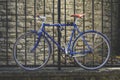 Blue Retro Bicycle Parked Against Metal Fence With Brick Wall Background. Vintage Bicycle
