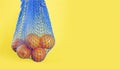 Blue reusable mesh bag with oranges hanging on a yellow background. The concept of nature conservation, reuse and recycling.